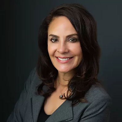 Cozakos and Centeno : Professional portrait of a smiling woman with medium-length dark hair, wearing a gray blazer, against a dark background.