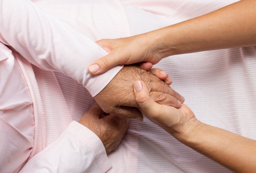 Cozakos and Centeno : A close-up of a younger person's hands holding an older person's hands, comforting them, both wearing light-colored shirts.