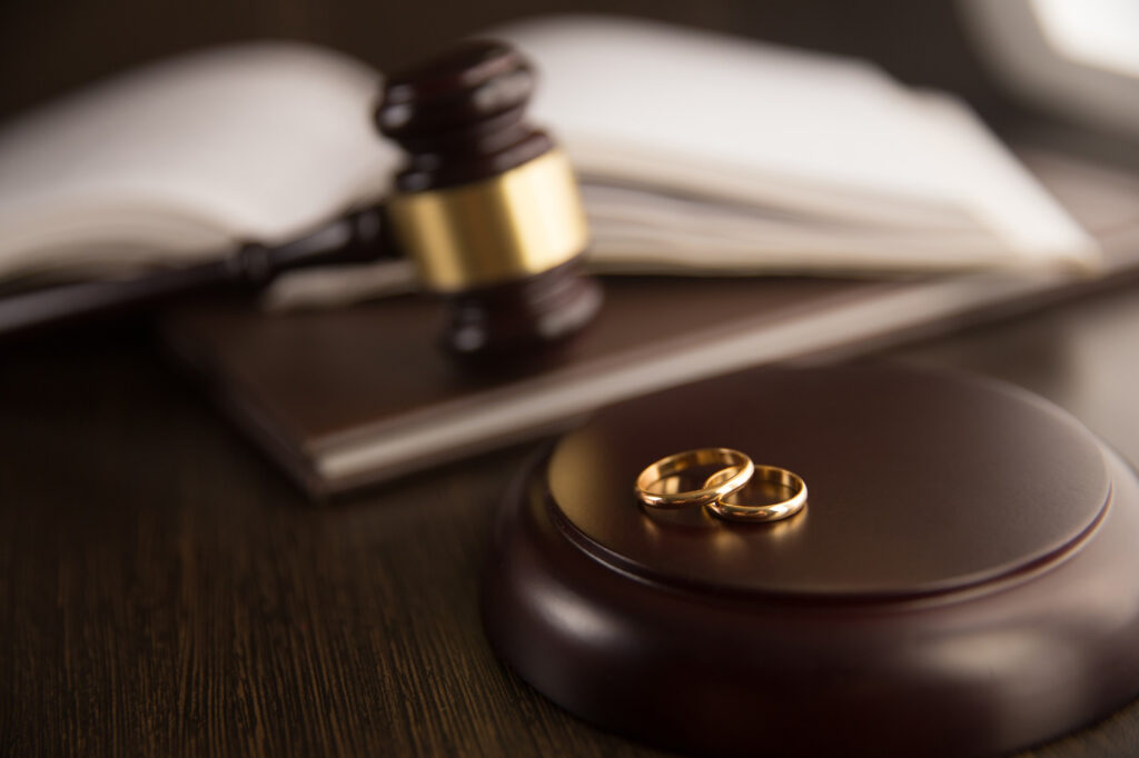 Cozakos and Centeno : A gavel on a wooden block beside two gold wedding bands, with an open law book in the background, symbolizing legal aspects of marriage.